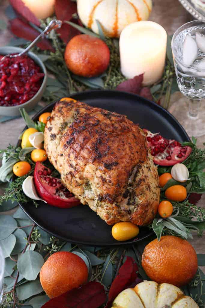 brined turkey breast on a black plate surrounded by herbs and kumquats, plus mini pumpkins and candles.