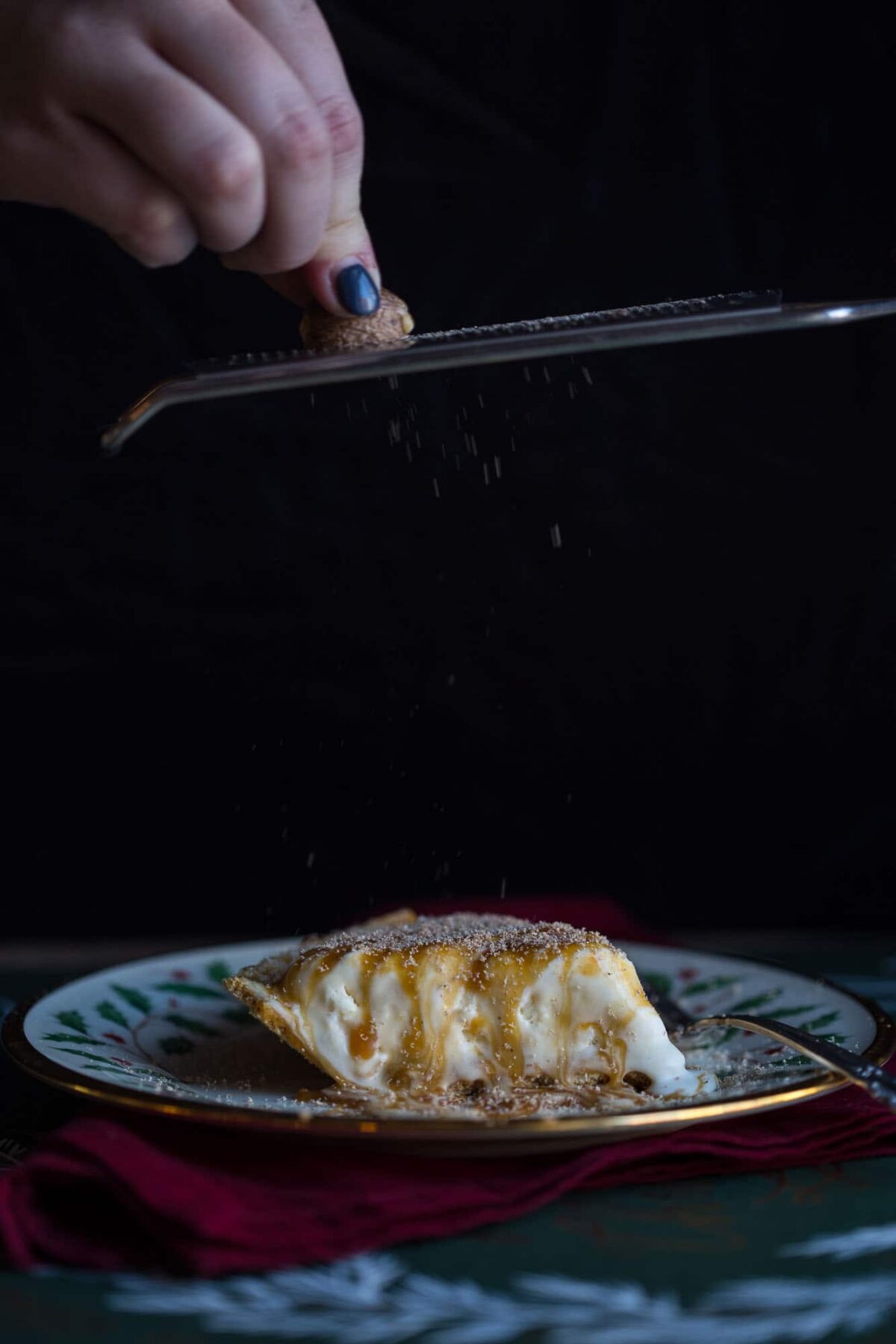 hand grating nutmeg on top of a slice of eggnog pie.