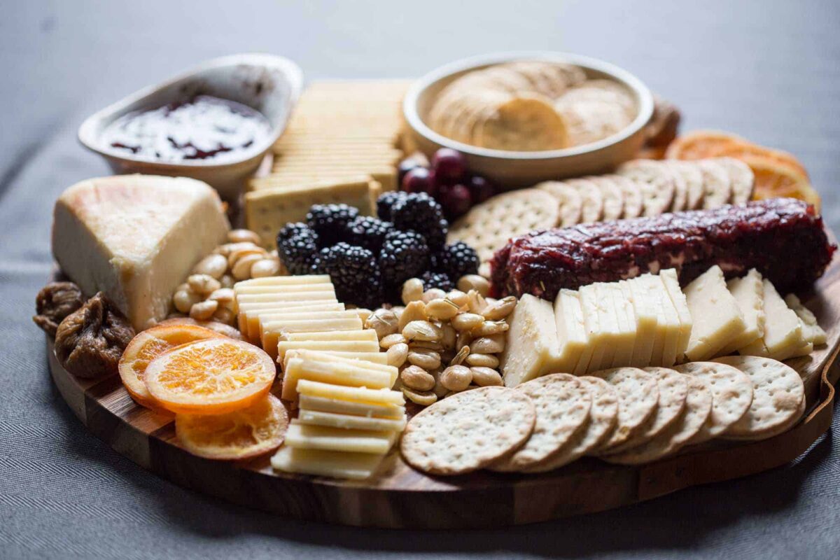 cheese, nuts, fruit, and crackers on a round wooden platter.