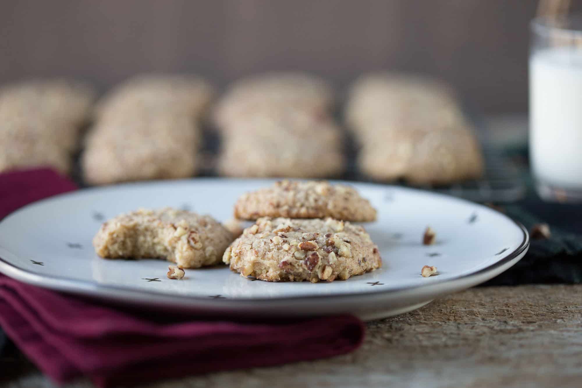 do re mi cookies on a white plate with more cookies and milk in the background.