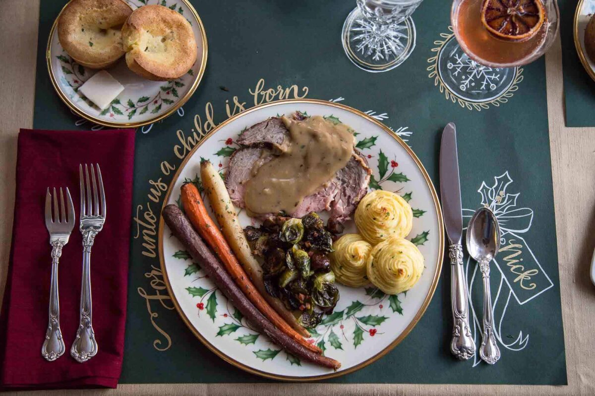 white china plate with prime rib, duchess potatoes, and roasted carrots on a green printed placemat.