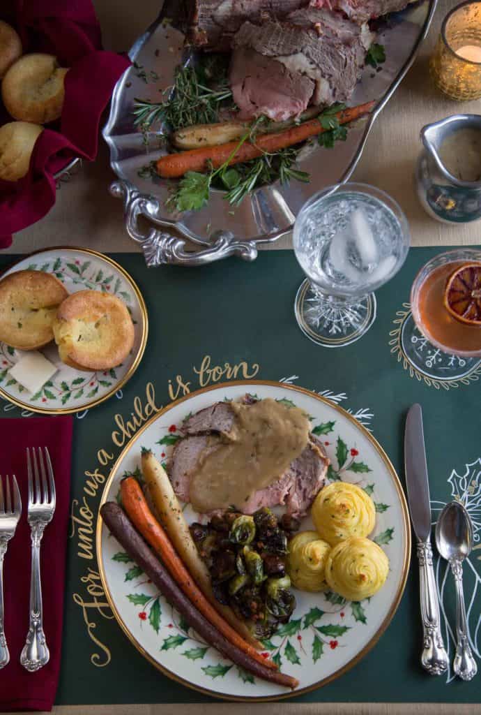 prime rib, duchess potatoes, and carrots on a dinner plate, on a table set for a holiday dinner with a prime rib in the center.