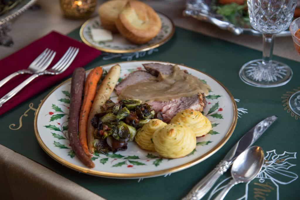 duchess potatoes, prime rib, and roasted carrots on a green and white china plate.