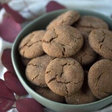 ginger cookies in a large green bowl with red leaves on the table underneath the bowl.