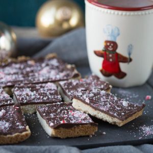 chocolate peppermint shortbread on a black cutting board with a gingerbread man tea cup in the background.