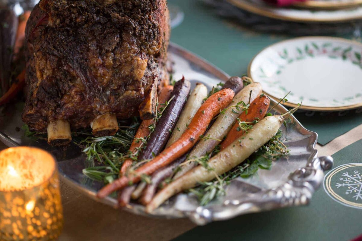 roasted carrots on a metal platter next to a prime rib.