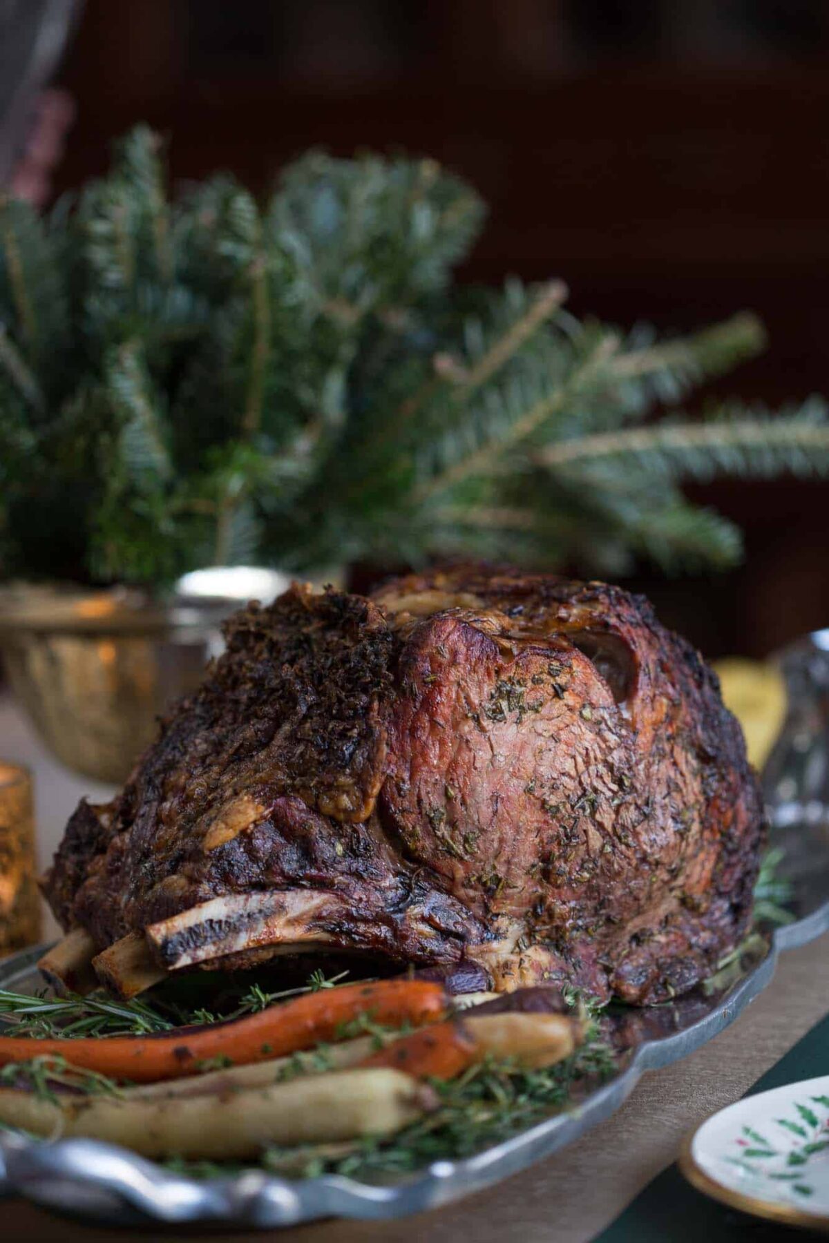 prime rib on a serving platter with roasted carrots, with greenery in the background.