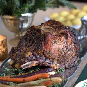 prime rib surrounded by herbs and roasted carrots sitting on a holiday table.