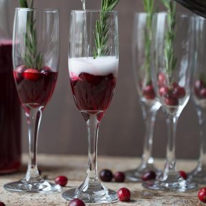champagne flutes filled with cranberry ginger prosecco cocktails and rosemary sprigs.