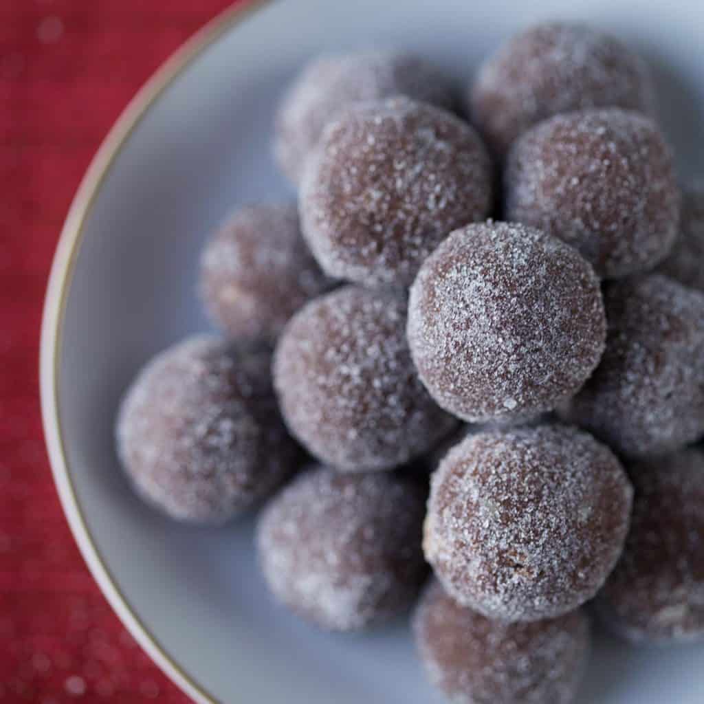 rum balls stacked in a white dish on top of a red tablecloth.