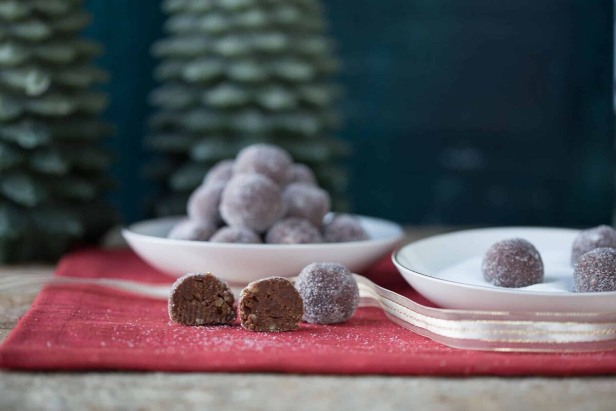 rum balls on a red placemat next to white bowls full of more rum balls.