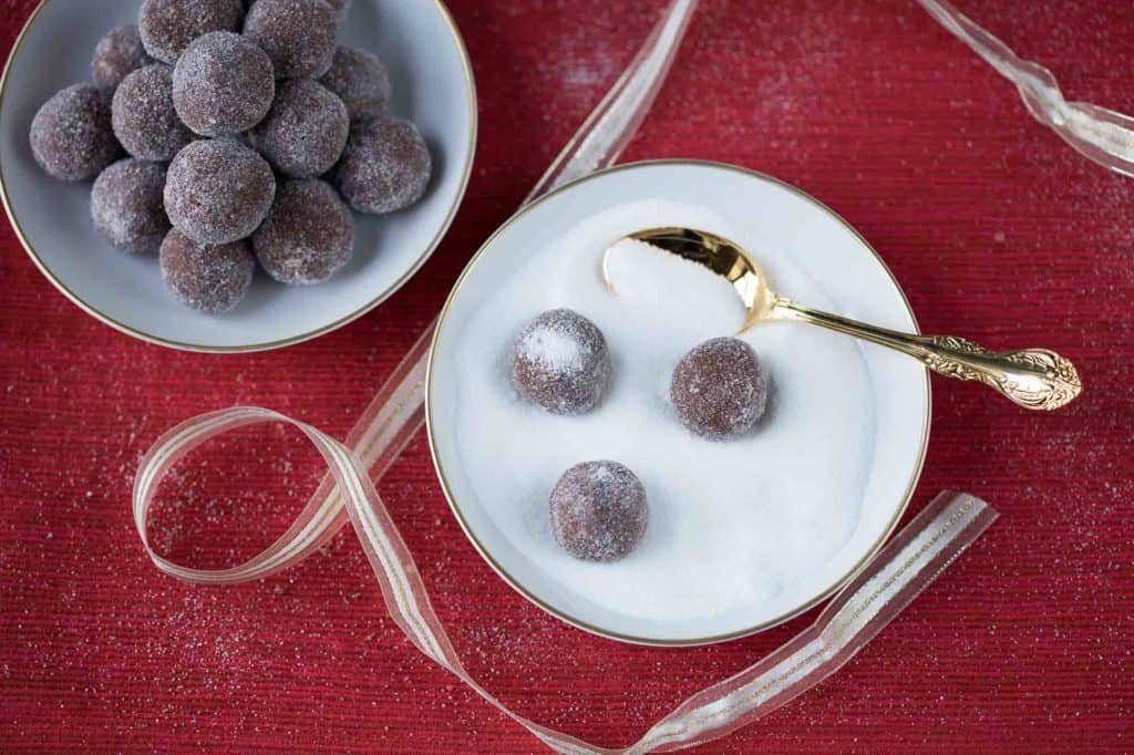 rum balls being rolled in granulated sugar in a small dish.