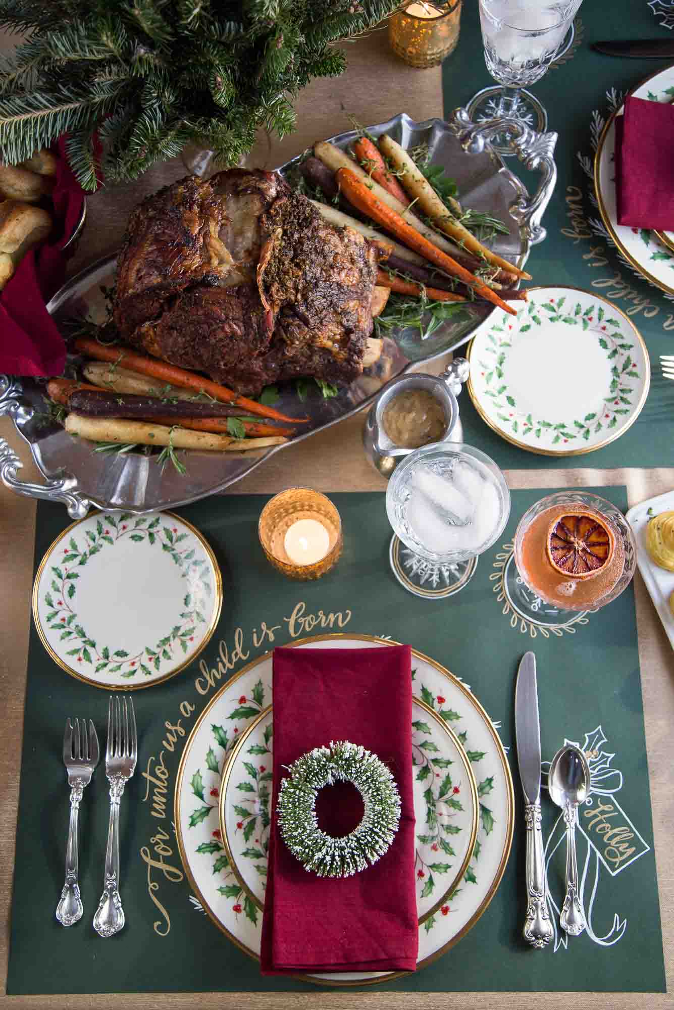 table set for christmas dinner with china, a red napkin, and a prime rib.