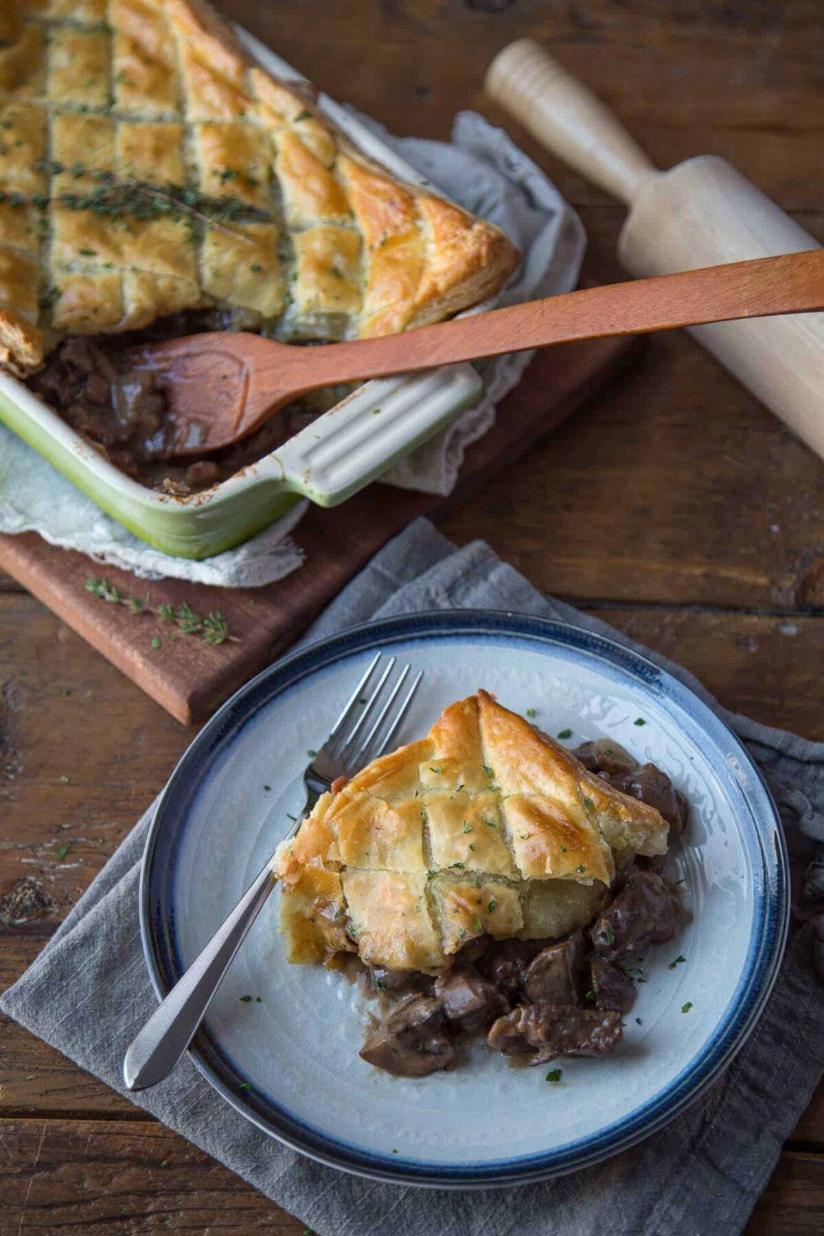 Beef Wellington Pot Pie on a plate with a full casserole dish and a wooden spoon.