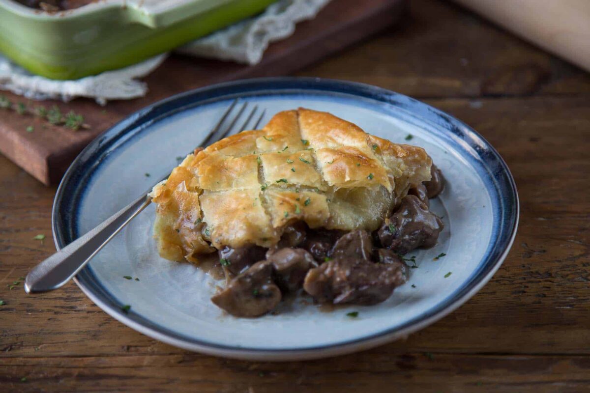 slice of beef wellington pot pie topped with puff pastry on a white and blue plate.