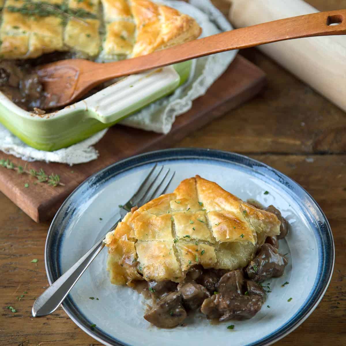 slice of beef wellington pot pie on a blue plate with more pot pie in the background.