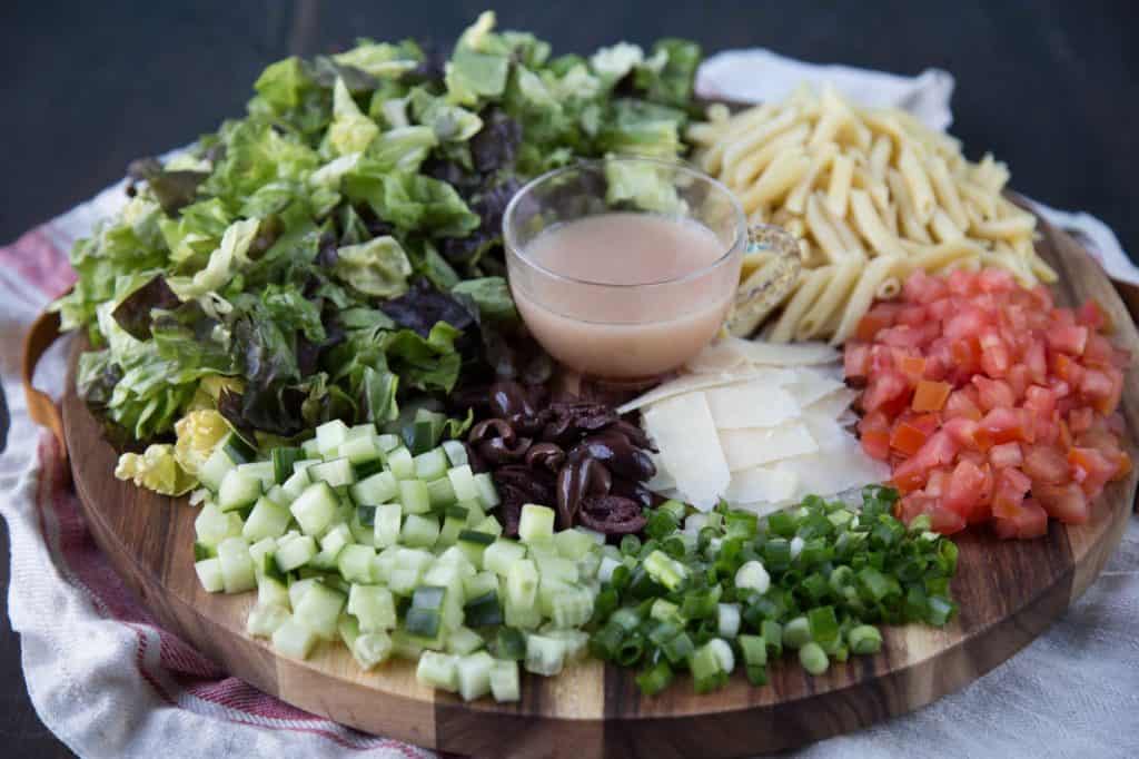 ingredients for an italian chopped salad on a round wooden board