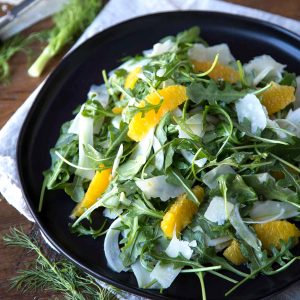 fennel and arugula salad with orange segments on a black plate.