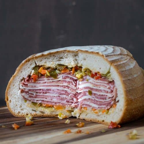 gigantic muffaletta cut open and sitting on a wooden board.