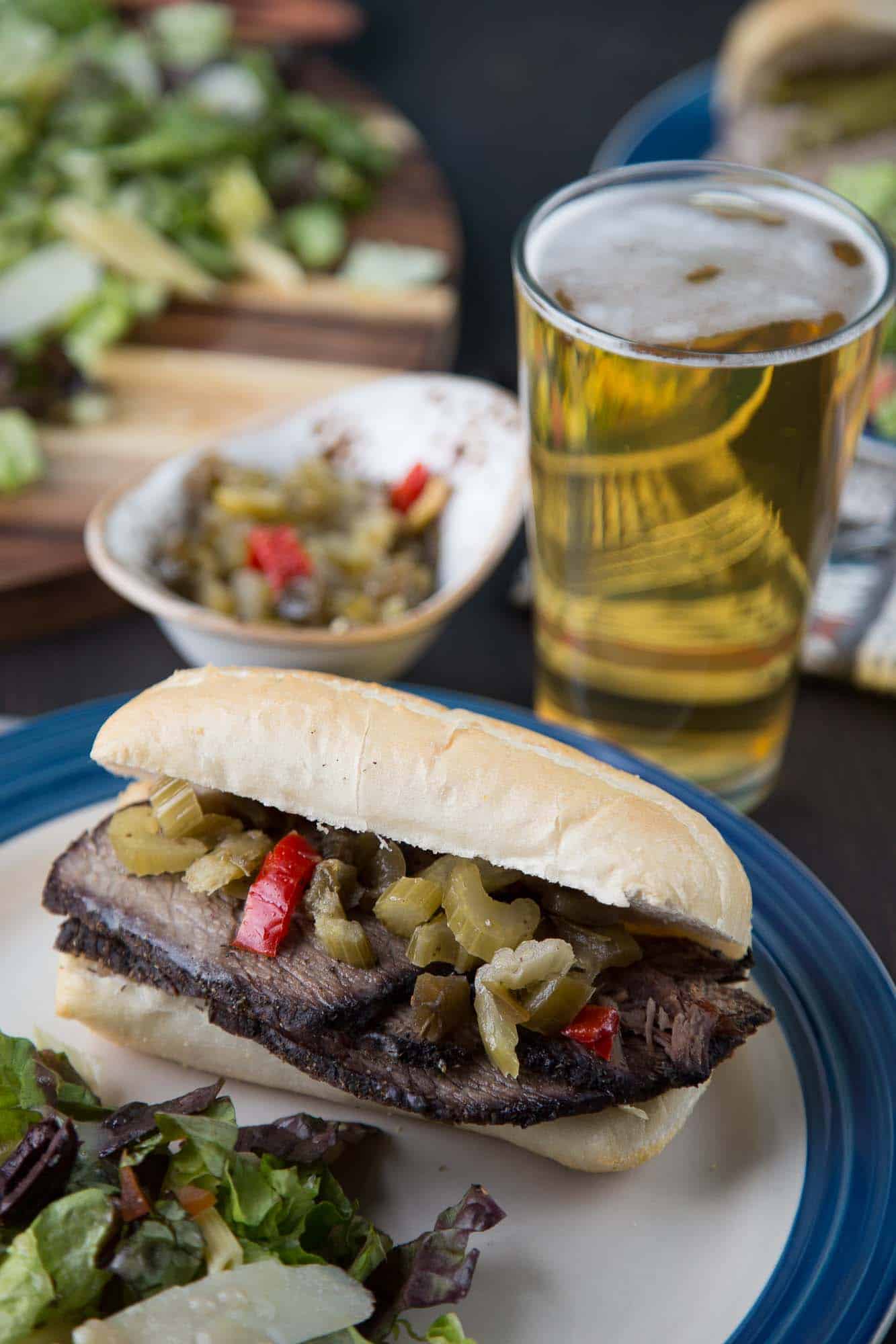 slow cooker italian beef on a white and blue plate, alongside a green salad and a pint of beer.