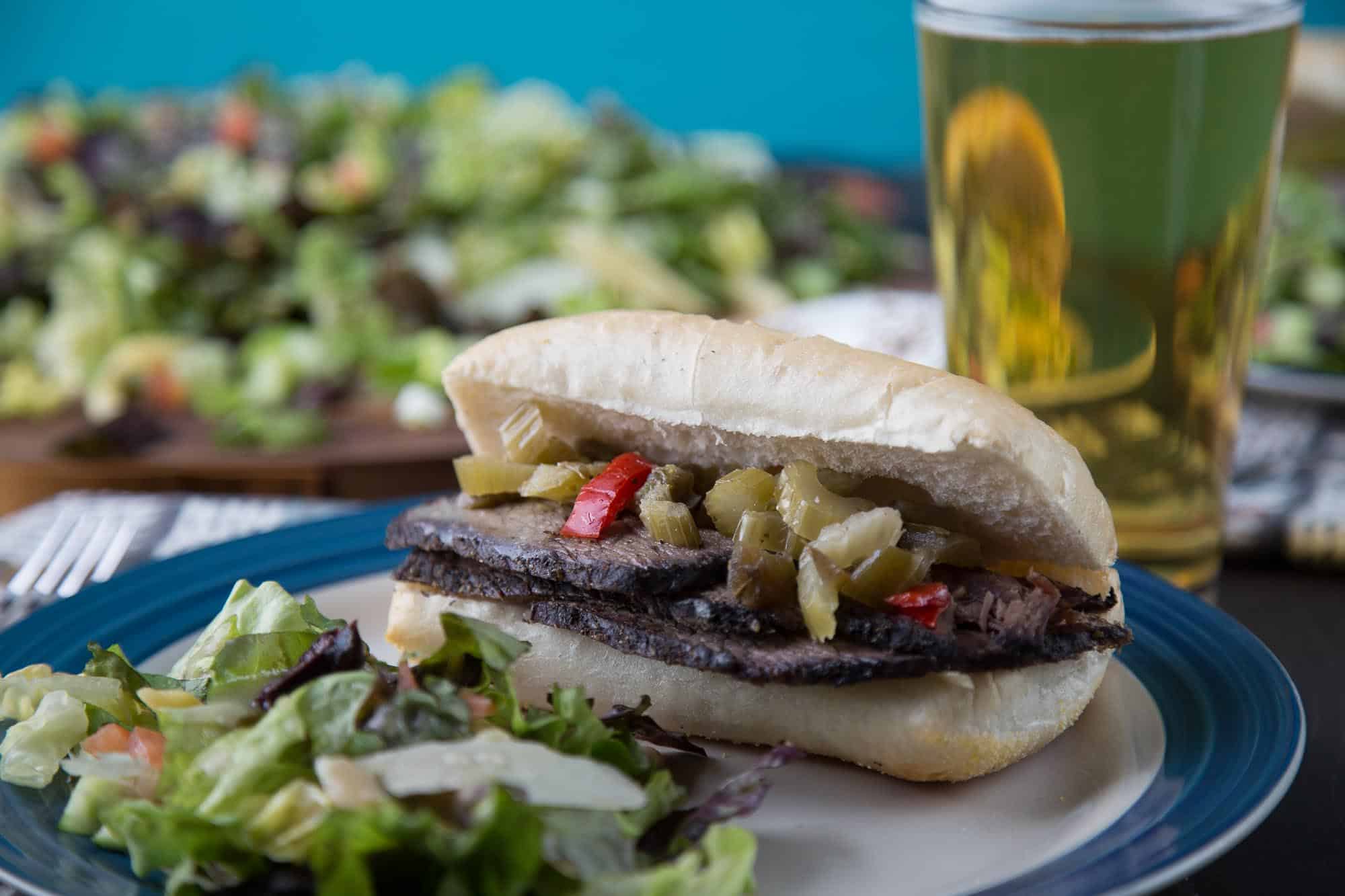 italian beef sandwich on a plate with italian chopped salad on the side.