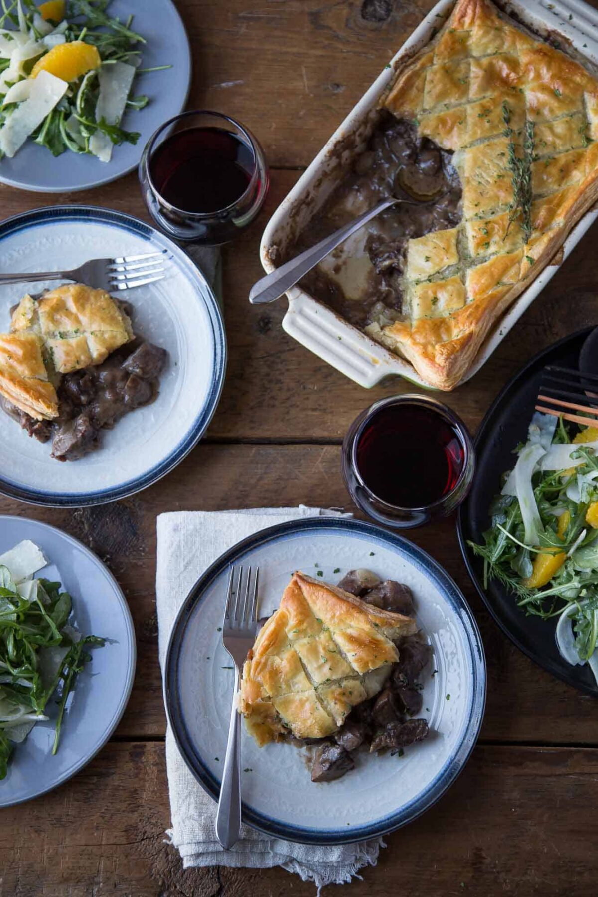 wooden table set for dinner with beef wellington pot pie and an arugula salad.