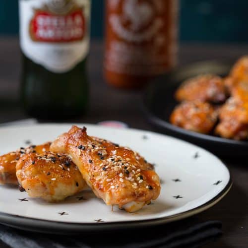 sweet and spicy wings on a black and white plate with a bottle of beer and more wings in the background.