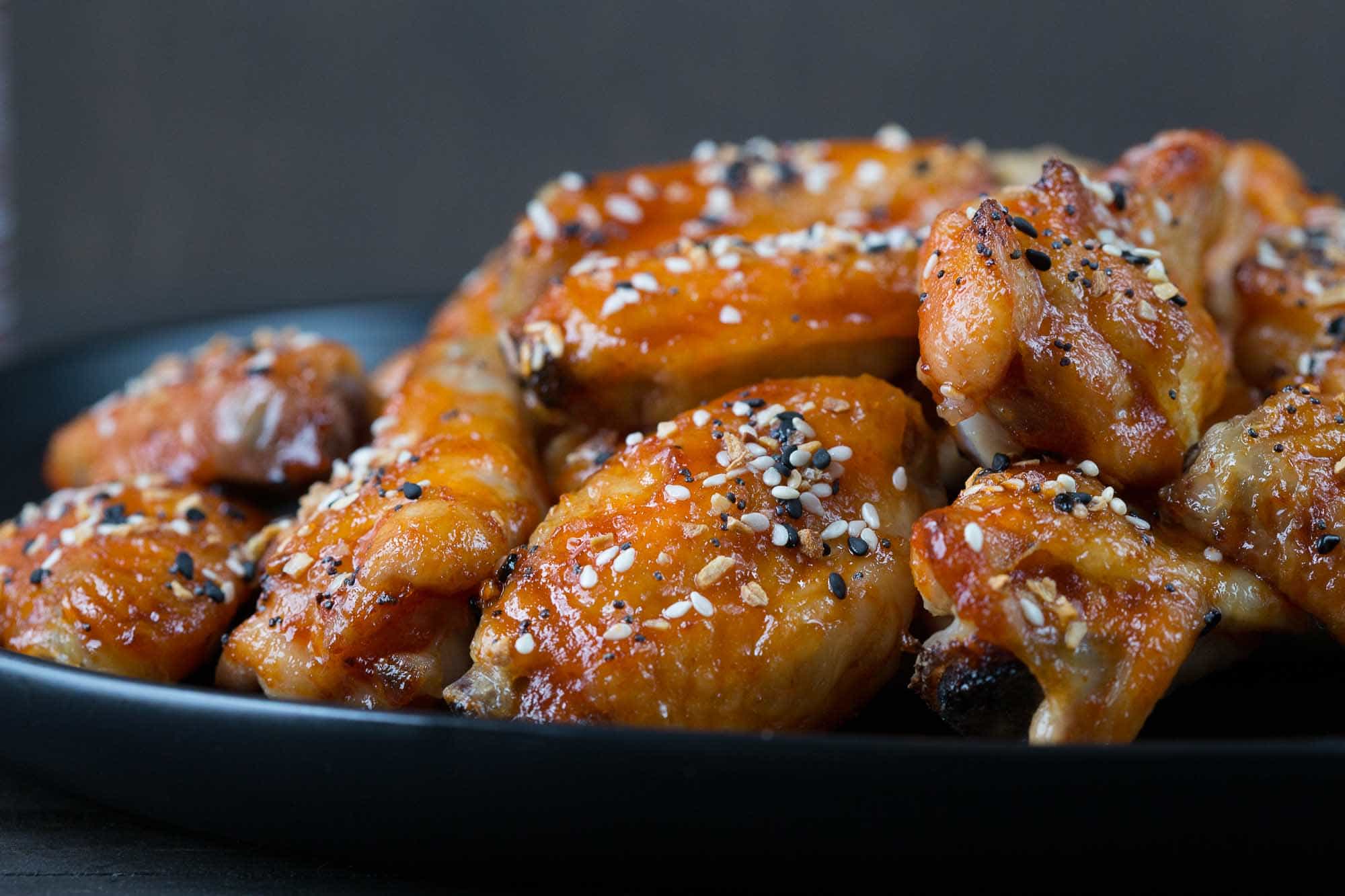 sweet and spicy chicken wings on a black platter.
