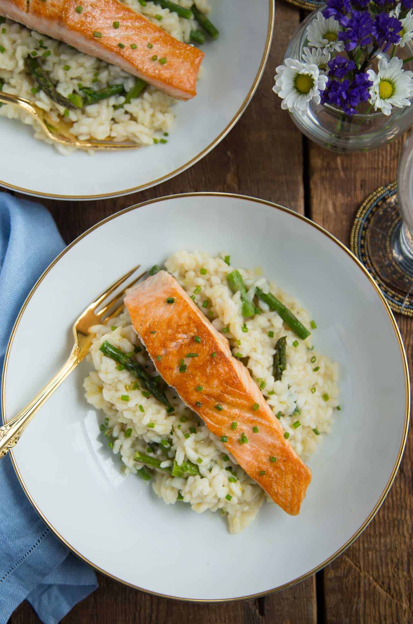 Seared Salmon over Asparagus Risotto on white china on a wooden table.