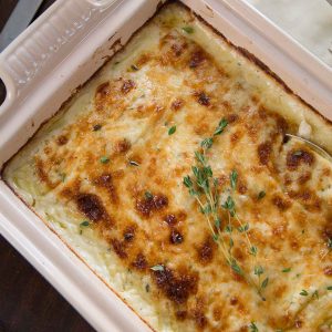scalloped potatoes topped with fresh thyme in a cream casserole dish.