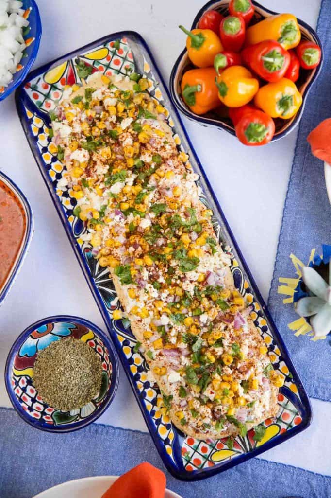 long rectangular platter of mexican street corn dip, surrounded by mini bell peppers.