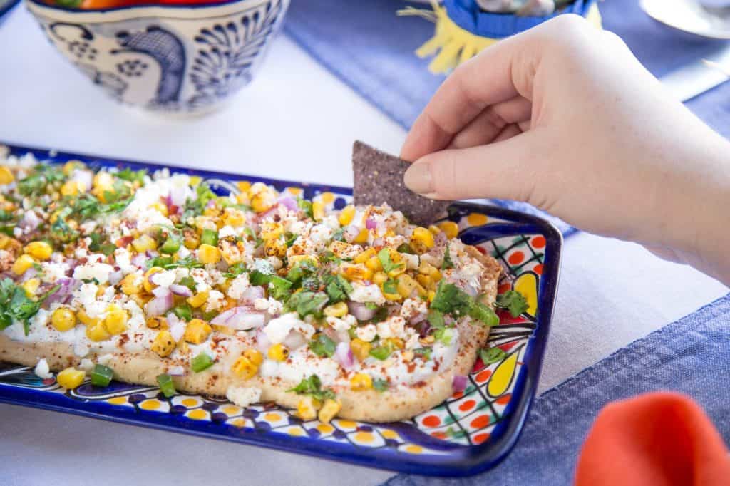 hand dipping a blue corn tortilla chip into mexican street corn dip.