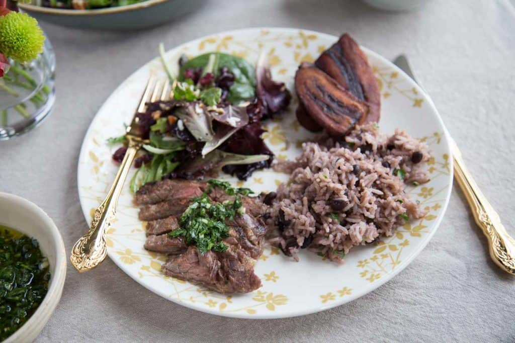 skirt steak, salad, arroz moro, and fried plantains on a dinner plate.