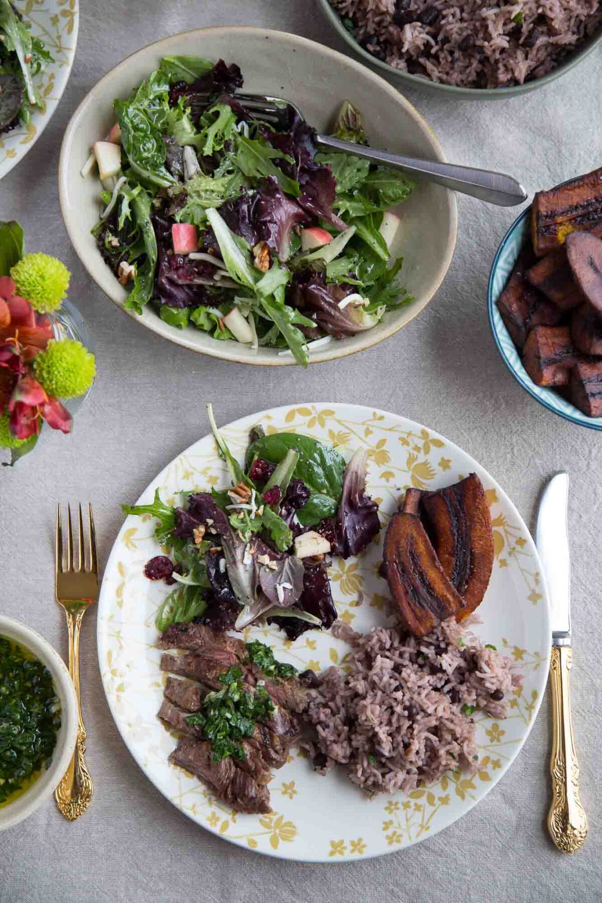 dinner plate with steak, rice, winter fruit salad, and plantains on a dinner table.