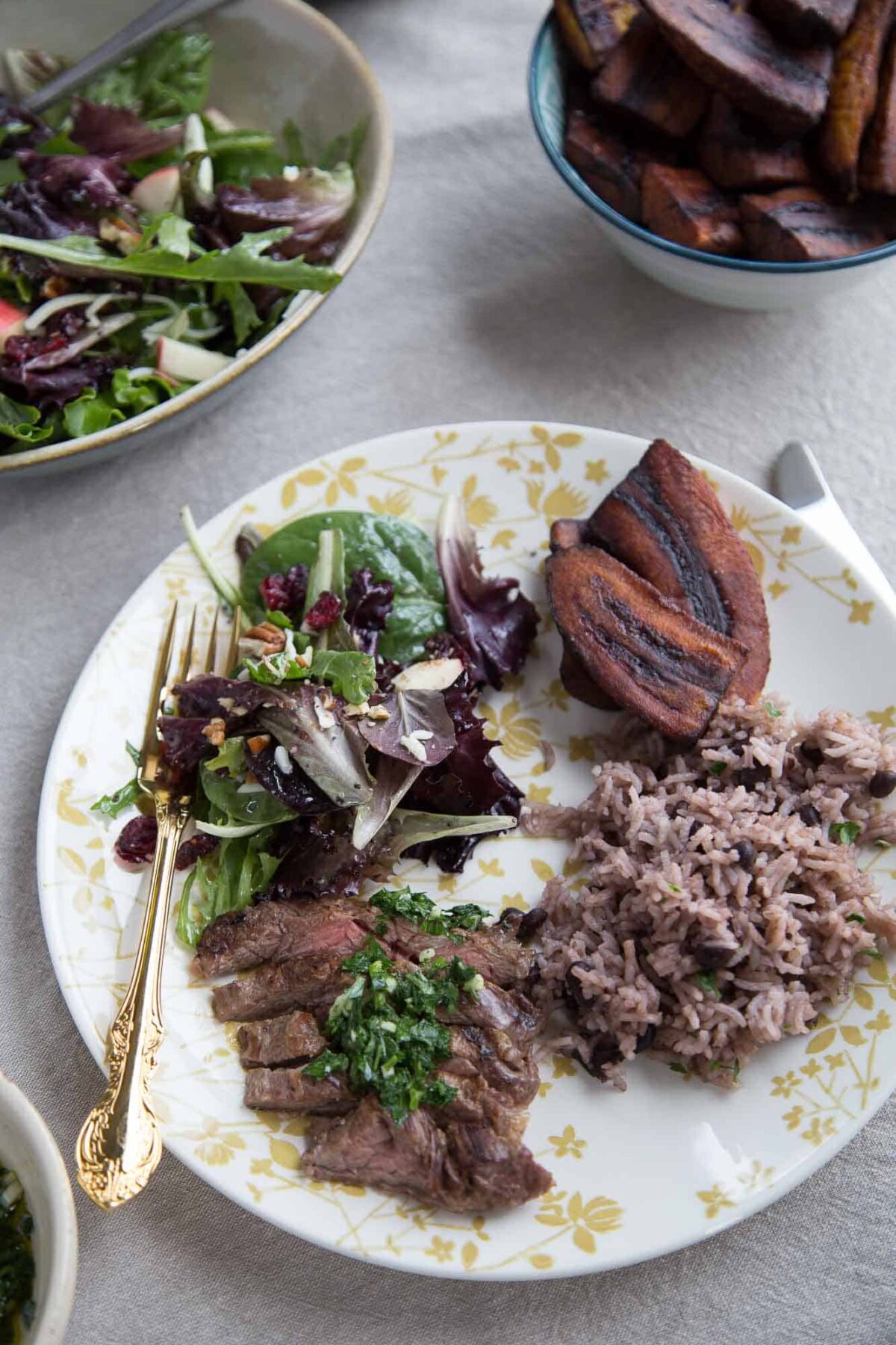 dinner plate with steak, cuban rice, plantains, and salad with a gold fork.