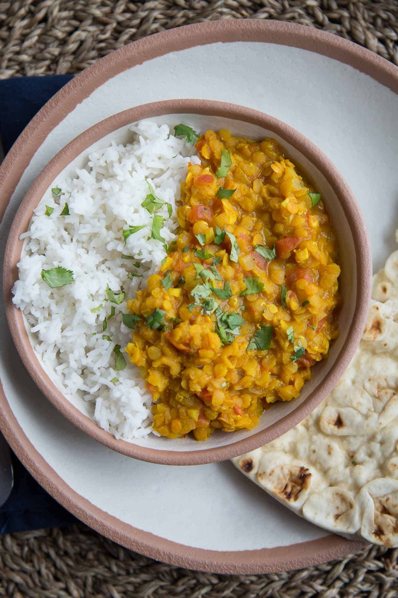 Vegetarian Red Lentil Dal in a brown rimmed bowl, with a side of rice and topped with cilantro.