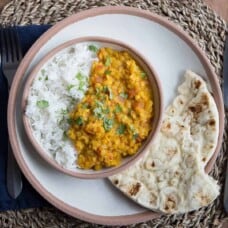 red lentil dal on a white plate with a side of naan, sitting on a woven placemat.