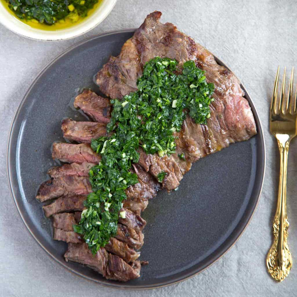 sliced skirt steak on a gray plate, topped with chimichurri sauce.