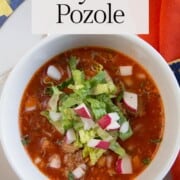 red pozole in a bowl topped with romaine and radishes.