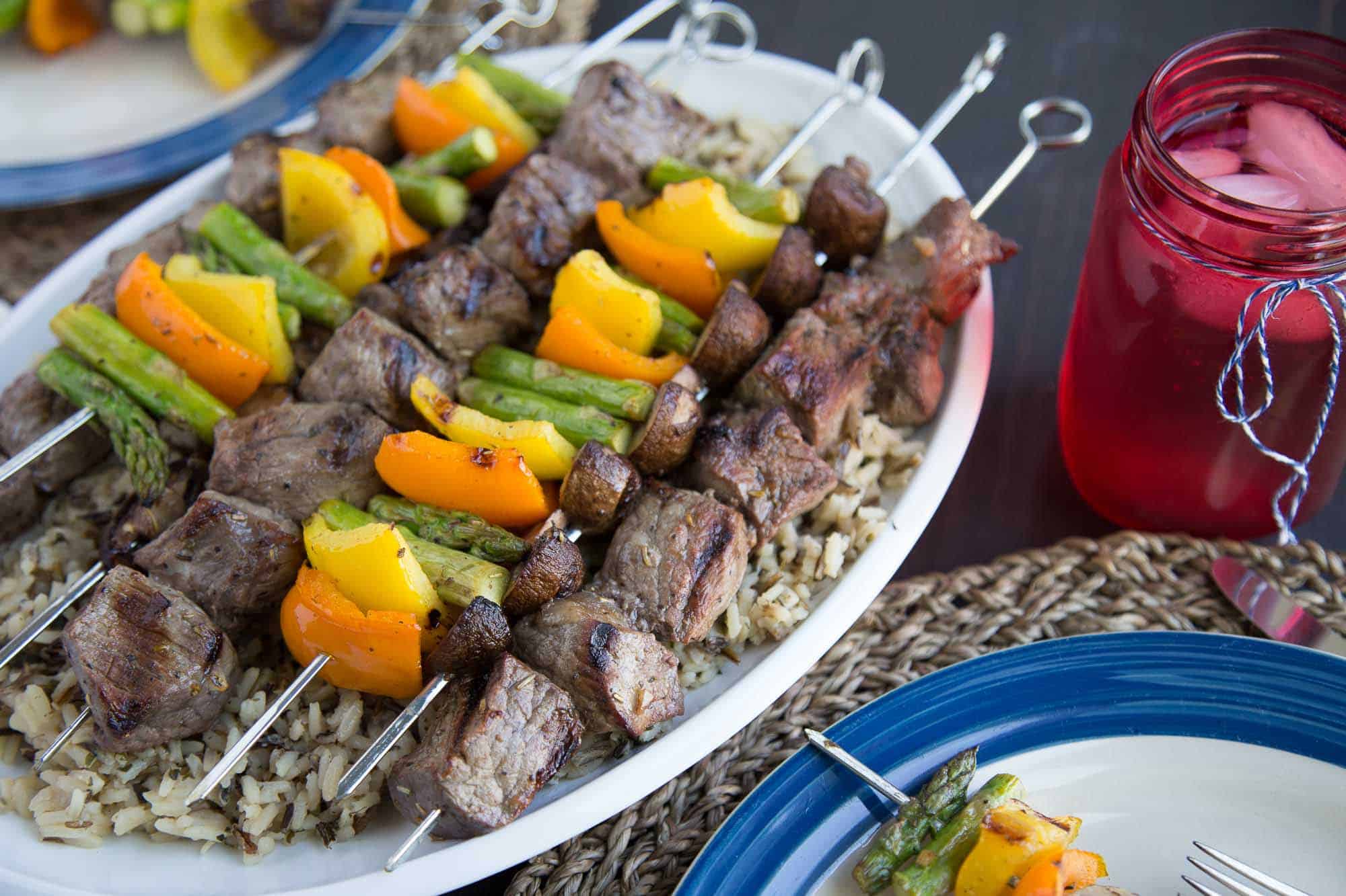 Italian Marinated Steak Kabobs on a white platter on a table set for dinner.