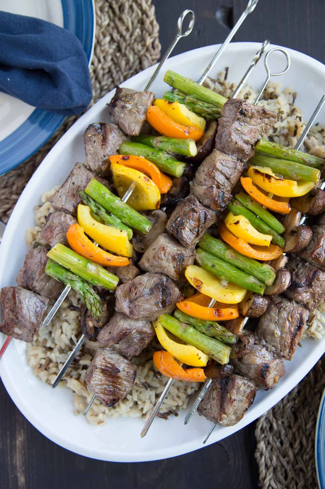 steak and veggie kabobs on top of wild rice, sitting on a white serving platter.