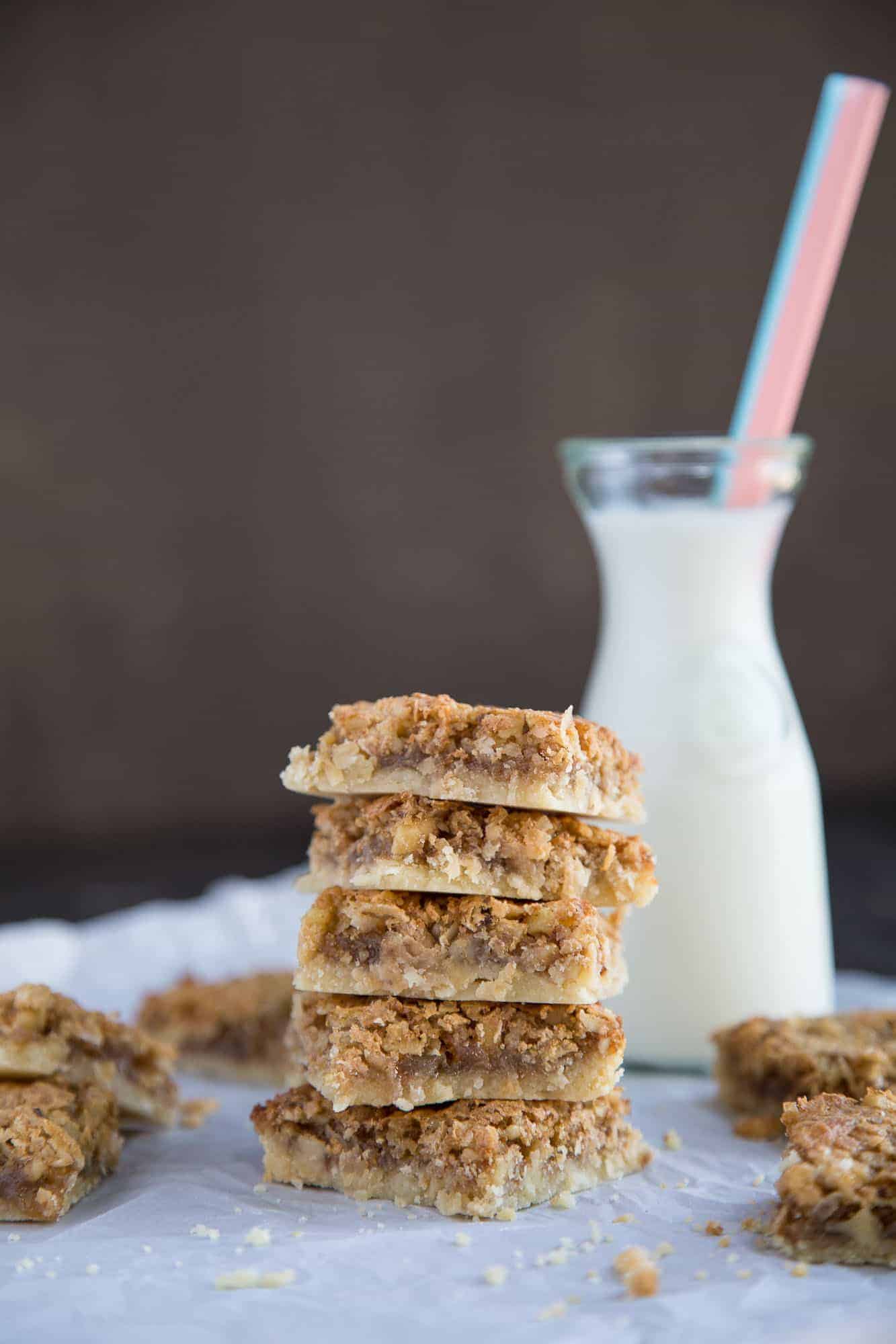 chewy coconut bars stacked on top of one another with a glass of milk in the background
