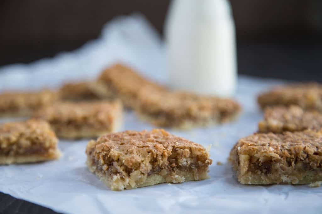 chewy coconut bars on white parchment paper with a glass of milk in the background
