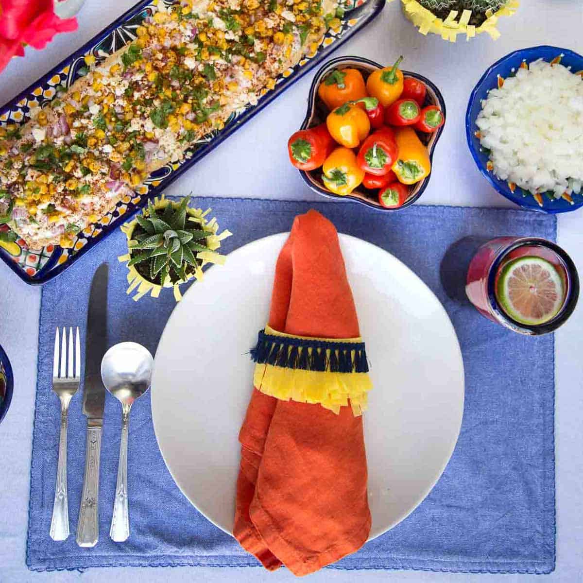 blue placemat topped with a plate and orange napkin with a colorful napkin ring.
