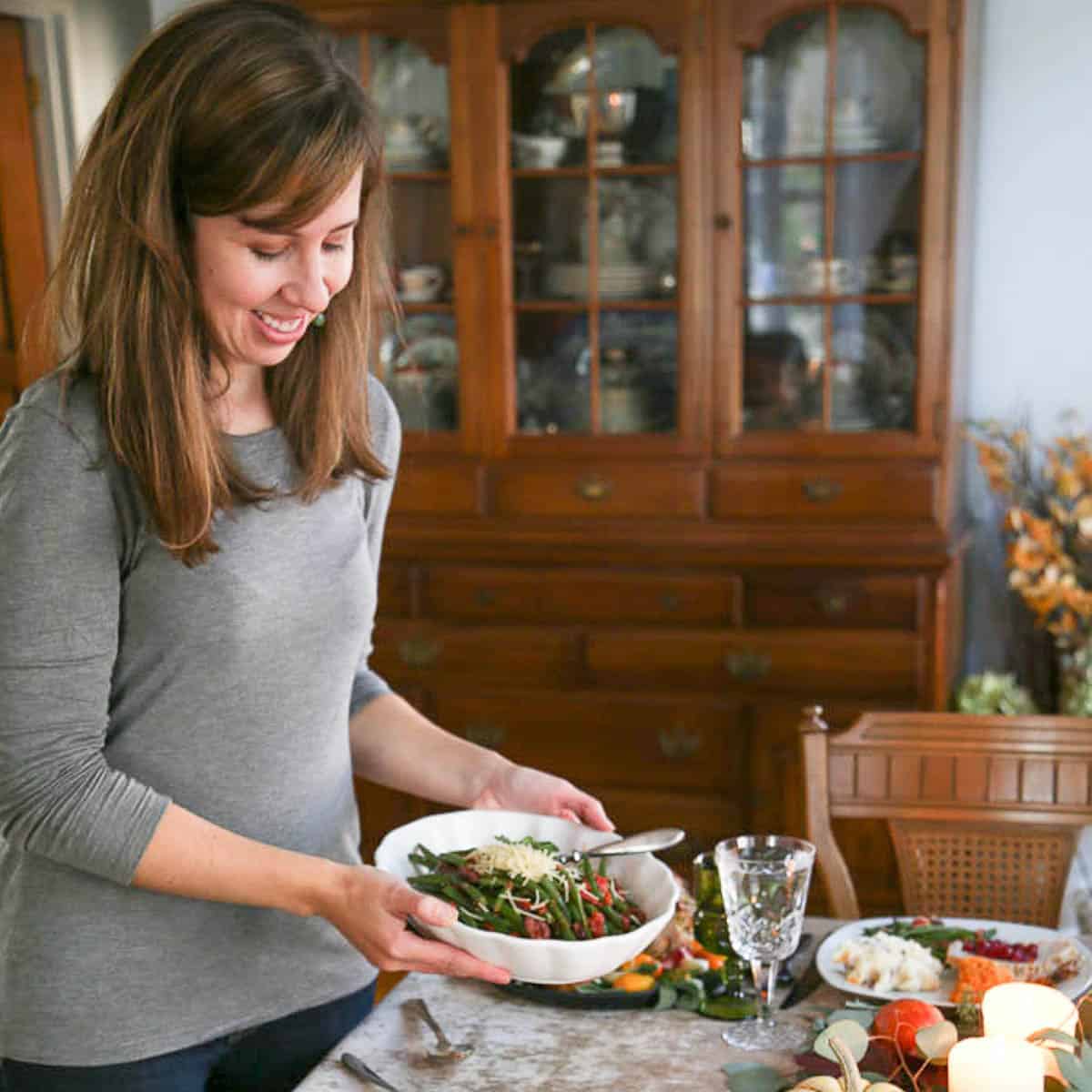 woman holding a bowl of green beans, about to set it on a dining table.
