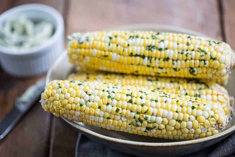corn on the cob with herb compound butter in a beige bowl.