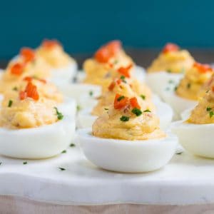 pimento cheese deviled eggs on a white marble platter with a blue background.