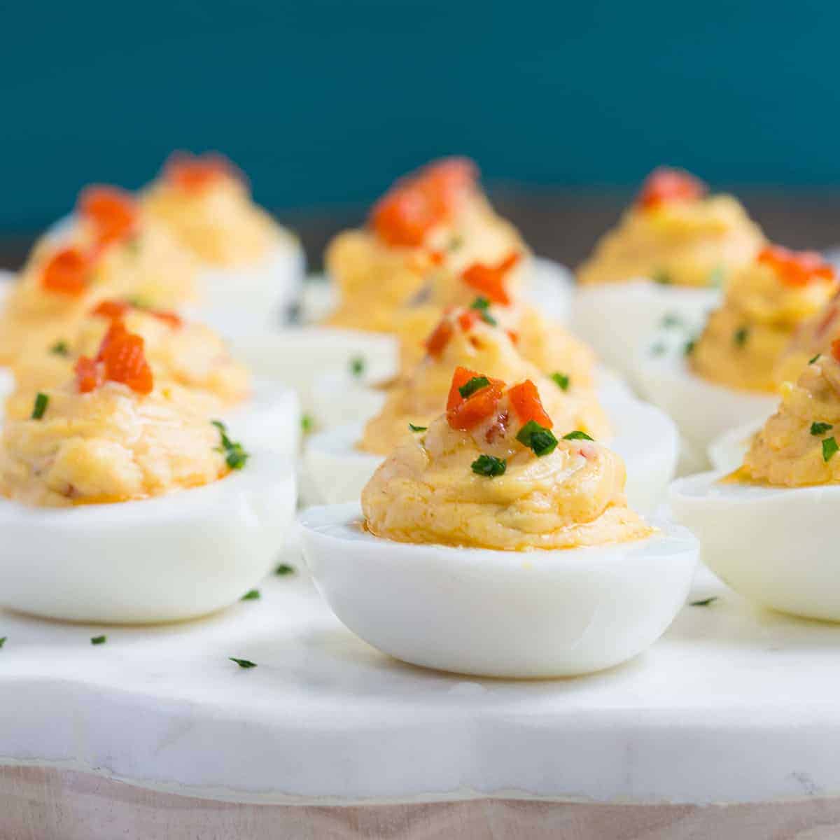 pimento cheese deviled eggs on a white marble platter with a blue background.