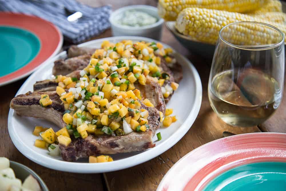 white platter of pork chops with peach salsa on a wooden table set for dinner