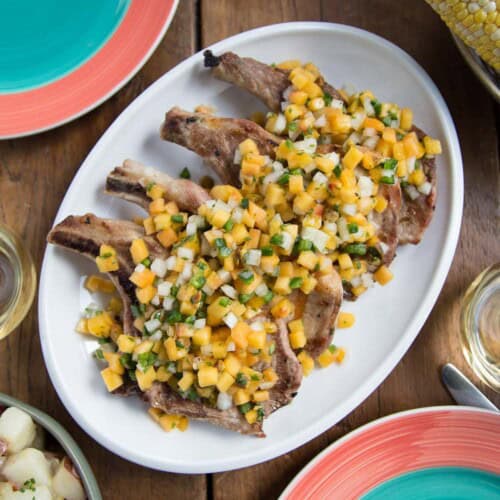 grilled pork chops topped with peach salsa on a white platter.